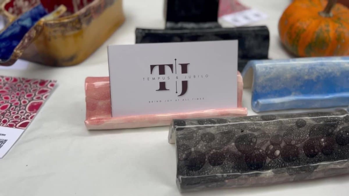 A handmade pink ceramic business card holder on the market table, holding a Tempus & Jubilo card, next to more of the maker's glazed pieces.