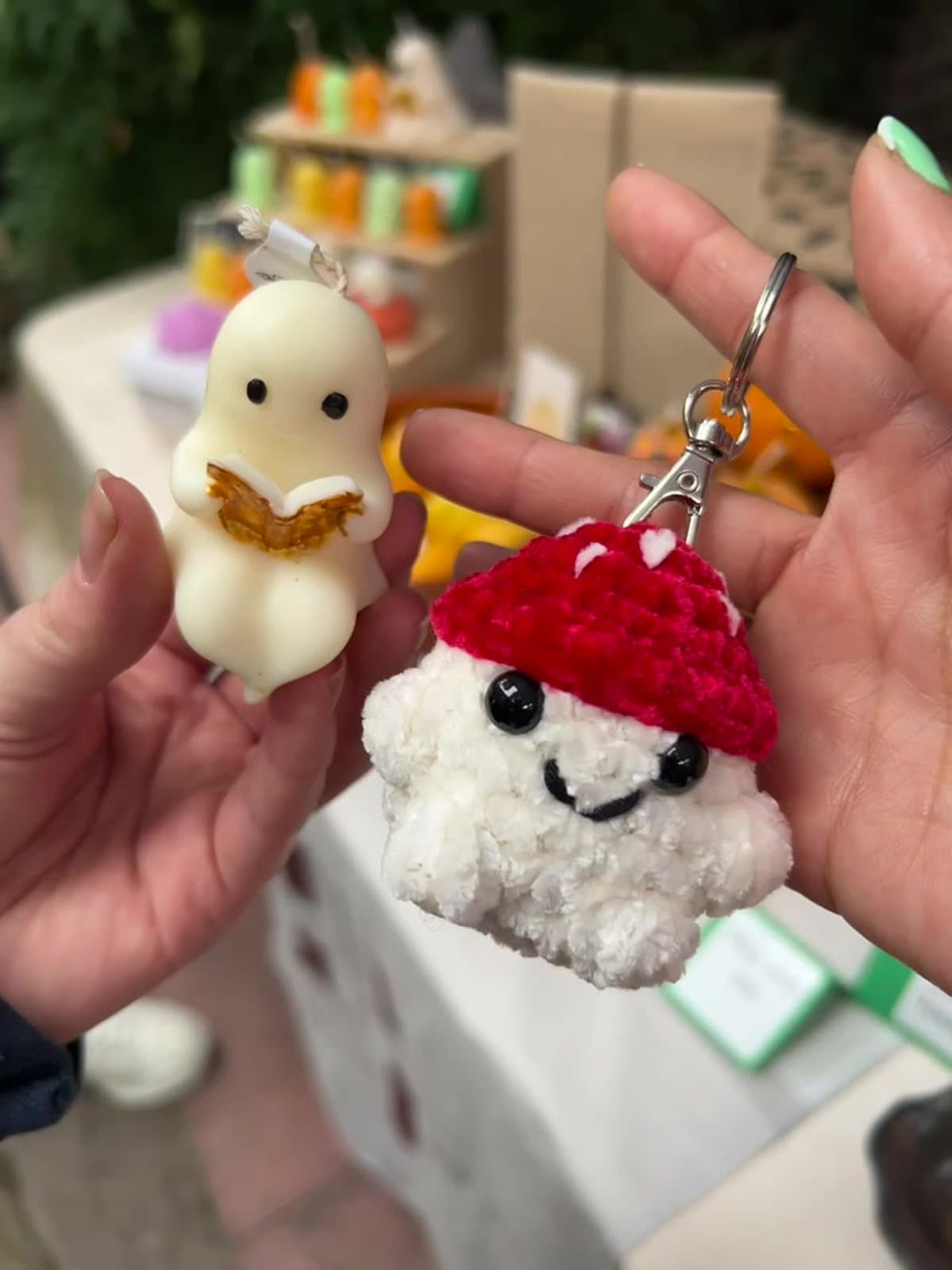 A small cream Little Ghost Reading candle held next to a crocheted mushroom keychain with a bright red spotted cap, at Camden POP Handmade.