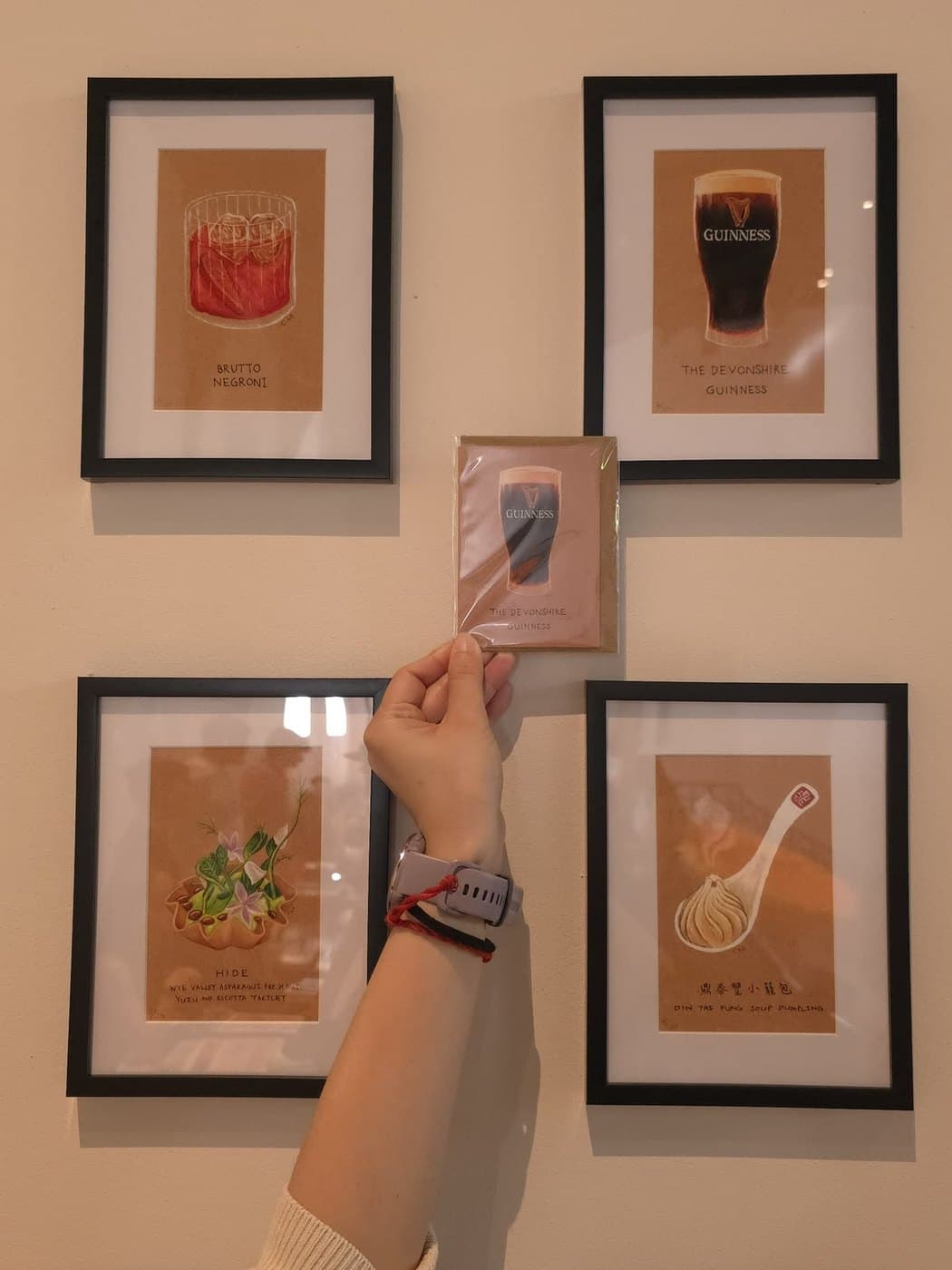 One of C.Lo's greetings cards, held up in front of her framed food and drink illustrations at the Food Art Fair