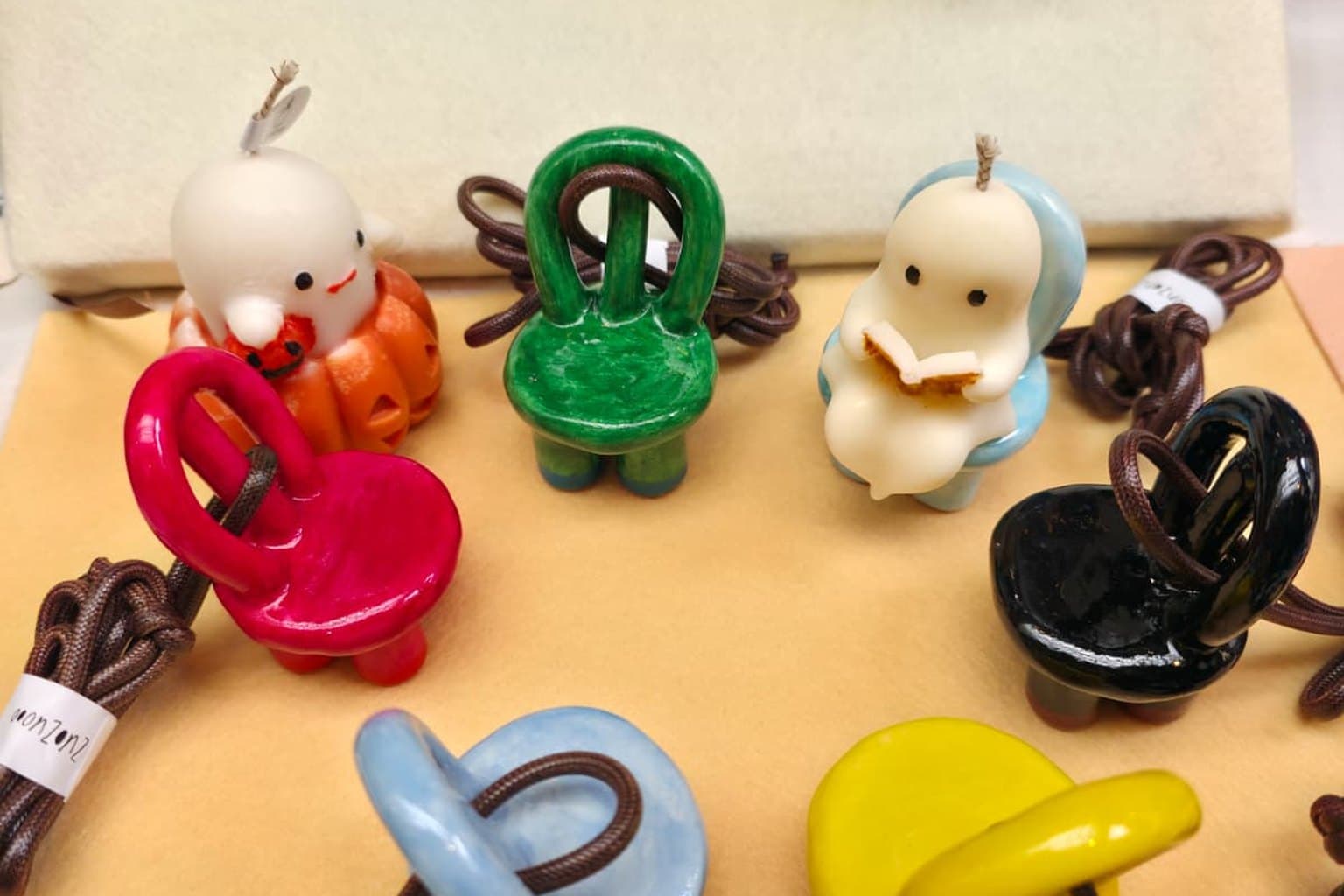 Little Ghost in a Pumpkin and Little Ghost Reading on a market table, among tiny ceramic chairs on brown cords in green, magenta, black, blue and yellow.